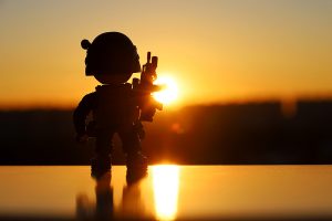 Silhouette of toy soldier on background of evening city and sunset sky. Concept of military forces, modern war