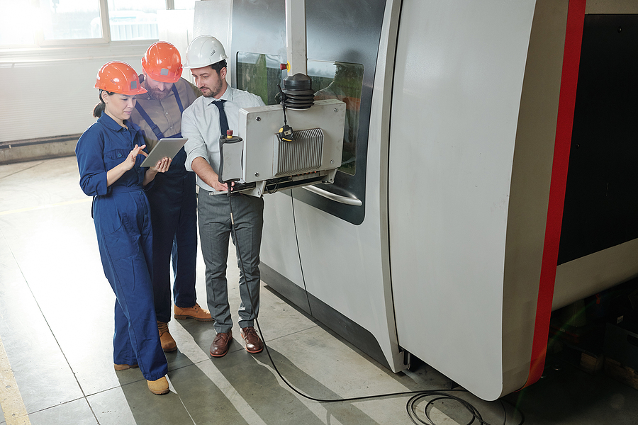 Engineers and programmer working with modern automated CNC machine in workshop