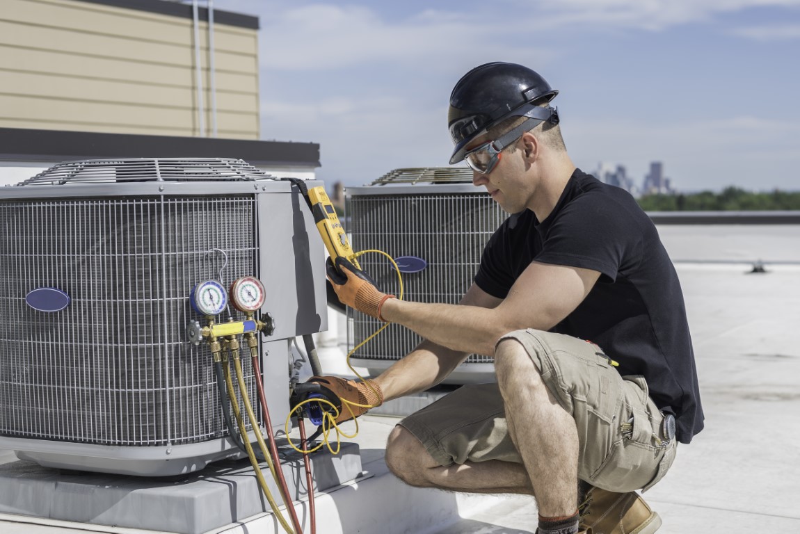 Hvac technician wearing safety gear inspecting an air conditioner