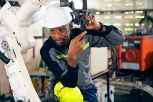 African American factory worker working with adept robotic arm in a workshop . Industry robot programming software for automated manufacturing technology .