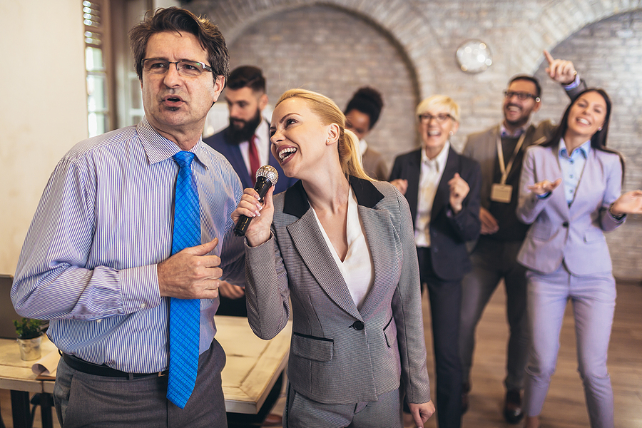 Business people having a karaoke party at the office, singing, dancing and having fun while taking a break from a busy work day