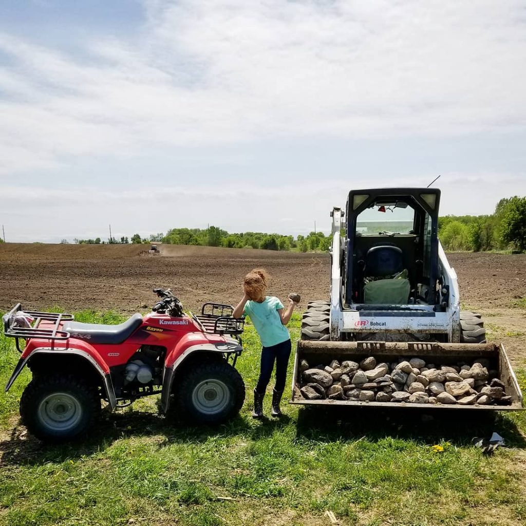 Iani by rocks piled in a skid standing by an ATV